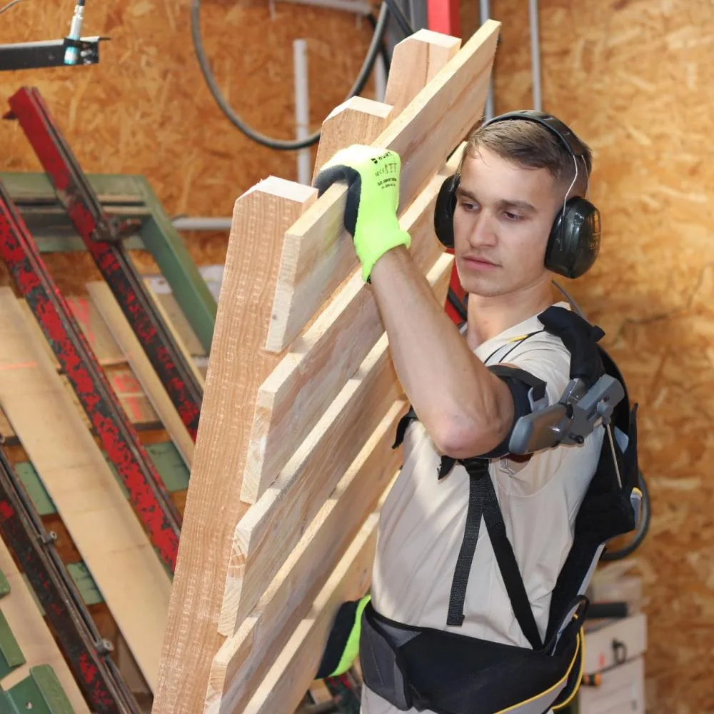 Opérateur équipé d'un exosquelette qui manipule des planches dans l'atelier de Janès Timber